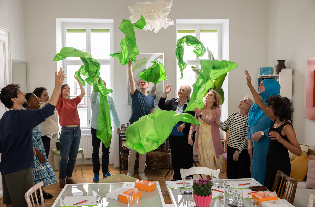 Eine Gruppe an Workshopteilnehmer:innen wirft grüne Seidenstücke in die Luft.